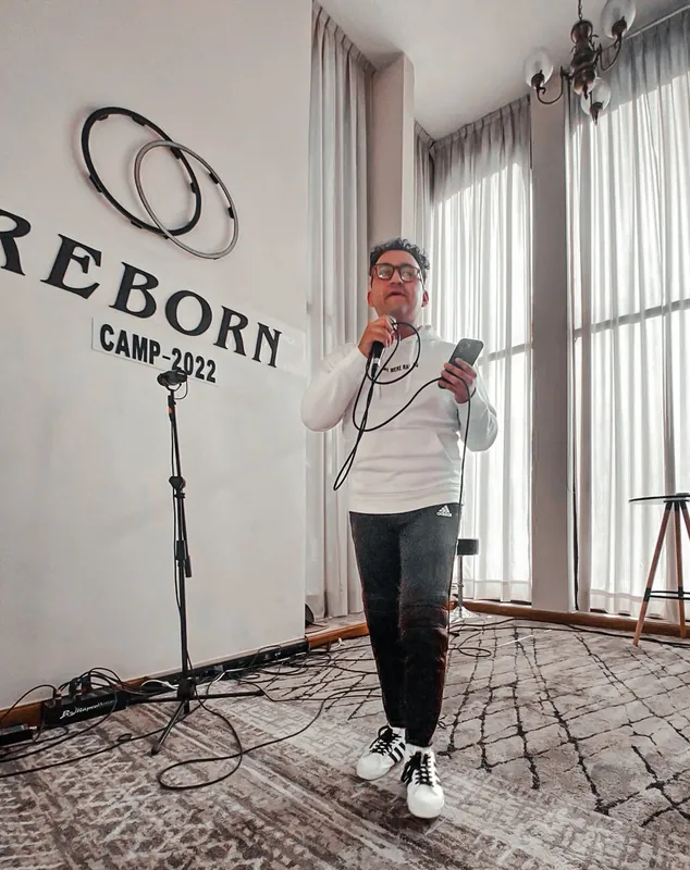 Predicador con micrófono frente al letrero de REBORN Camp 2022