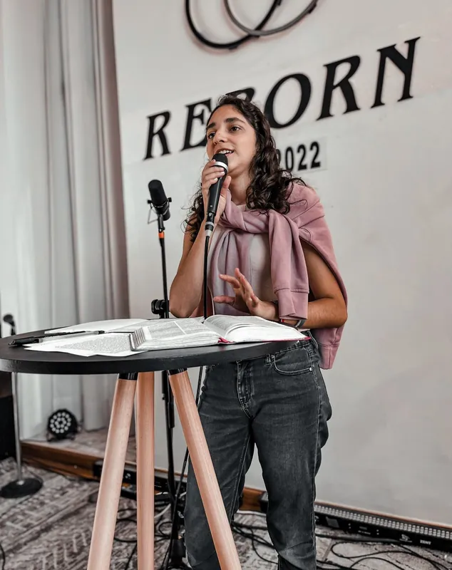 Joven predicadora con micrófono frente al letrero de REBORN 2022