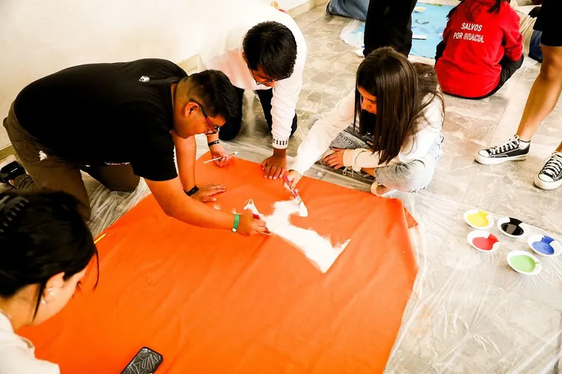 Jóvenes pintan una paloma sobre una bandera naranja
