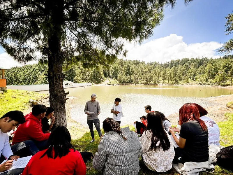 Jóvenes reunidos junto a un lago escuchan a un guía