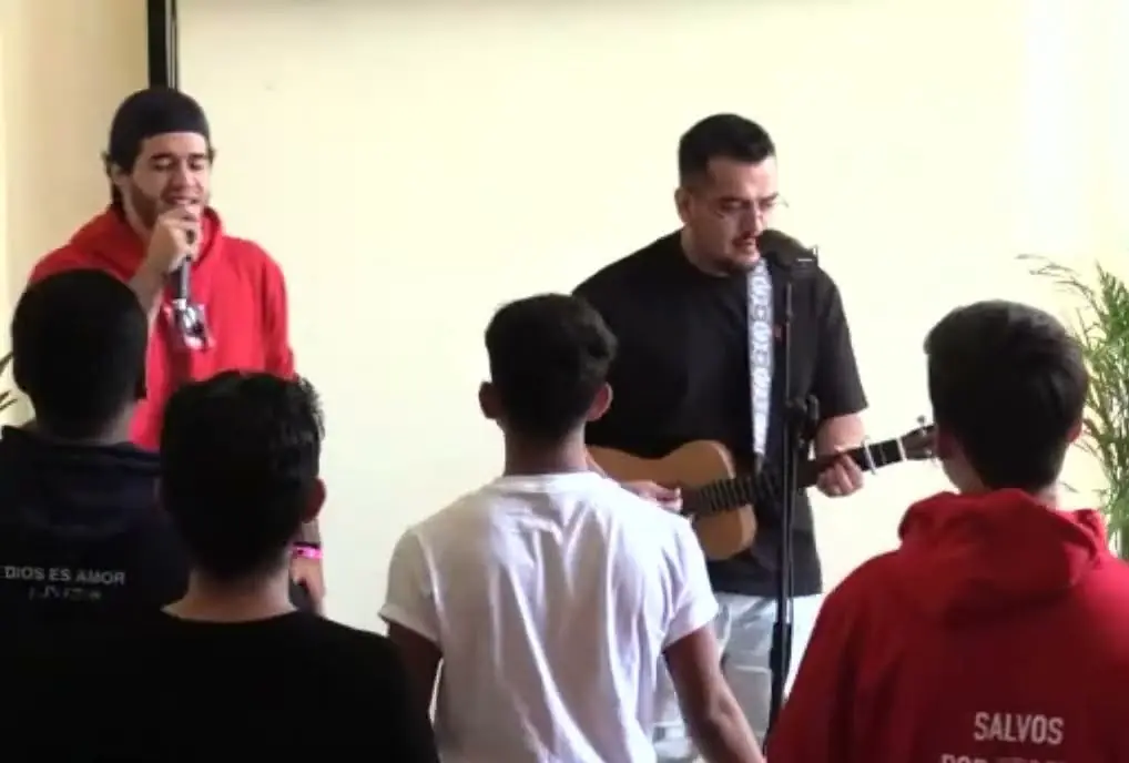 Jóvenes en la alabanza del tercer día de REBORN 2023, con guitarra; uno lleva una sudadera que dice «Salvos por gracia».