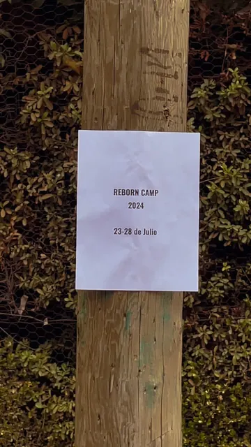 Letrero de REBORN CAMP 2024, del 23 al 28 de julio, pegado en un poste de madera.