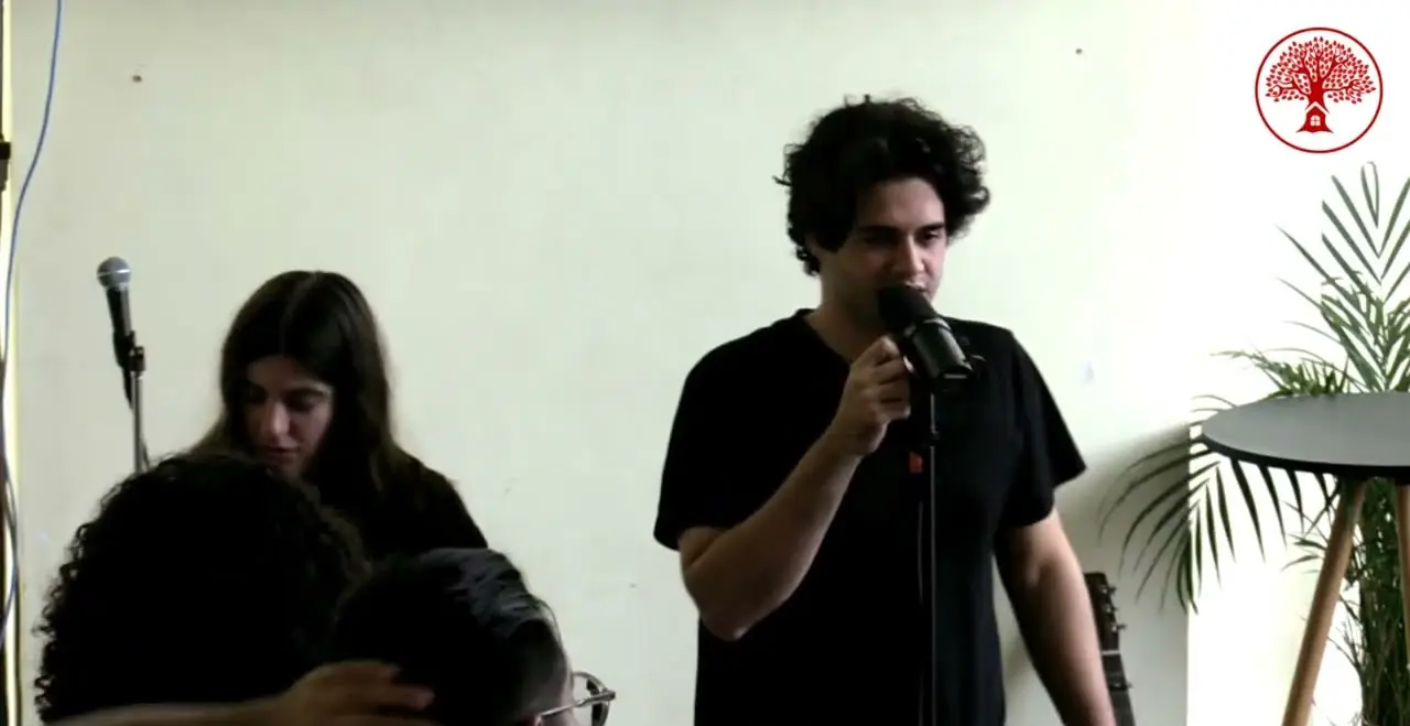 Un joven ora con el micrófono mientras una joven ora por otro joven, en REBORN 2024.