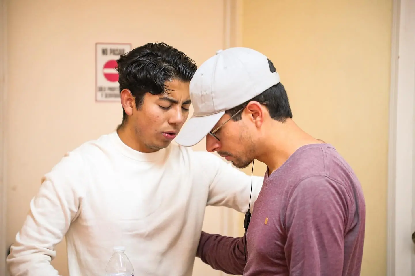 Dos jóvenes oran juntos con la cabeza inclinada.