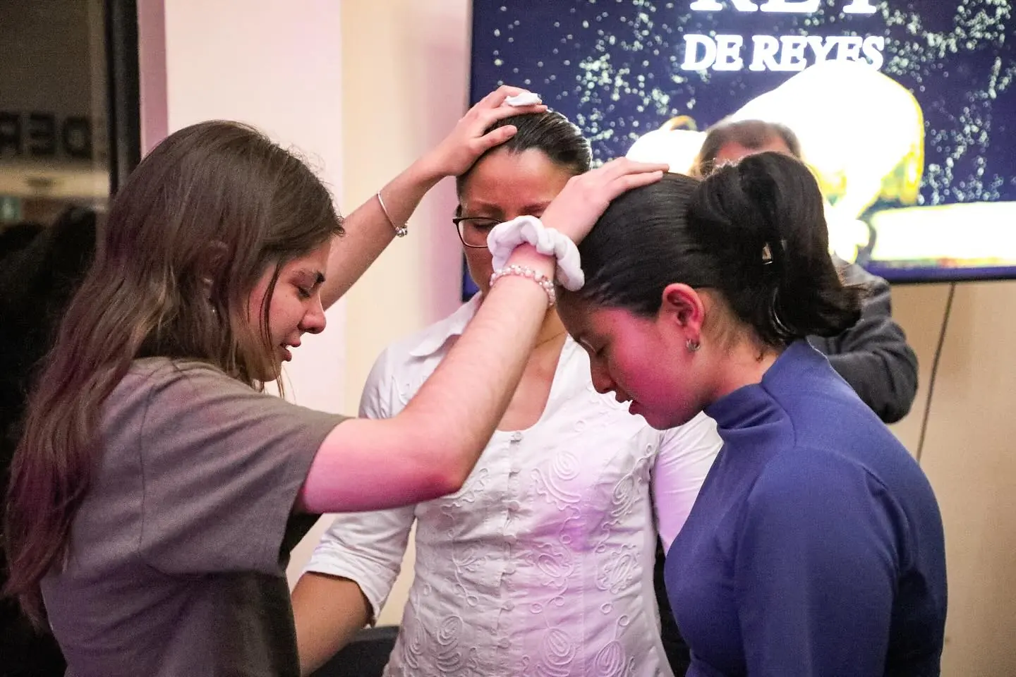 Una joven ora por una mujer y por una muchacha, con las manos sobre su cabeza.