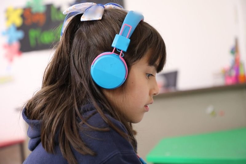 Una alumna de kínder con audífonos, atenta a su clase