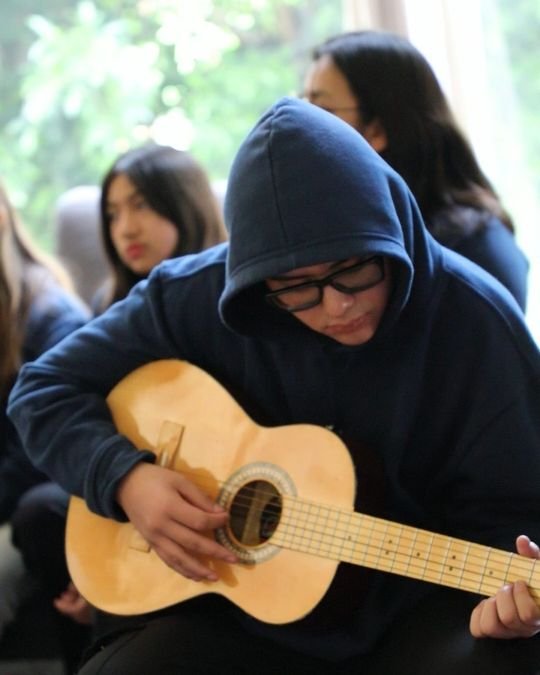 Un alumno de preparatoria toca la guitarra mientras sus compañeras escuchan