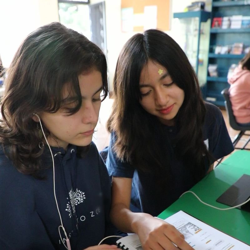 Dos alumnas de secundaria del Instituto Zoe leen juntas su cuaderno de inglés en su mesa