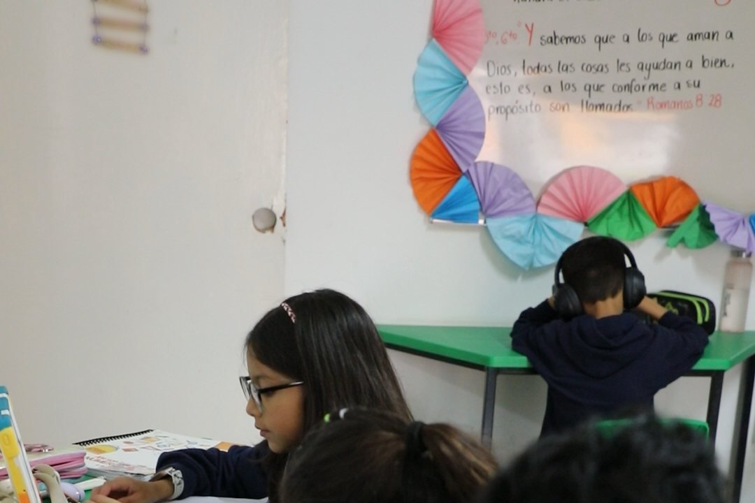 Clase de primaria del Instituto Zoe con Romanos 8:28 escrito en el pizarrón: «Y sabemos que a los que aman a Dios, todas las cosas les ayudan a bien»