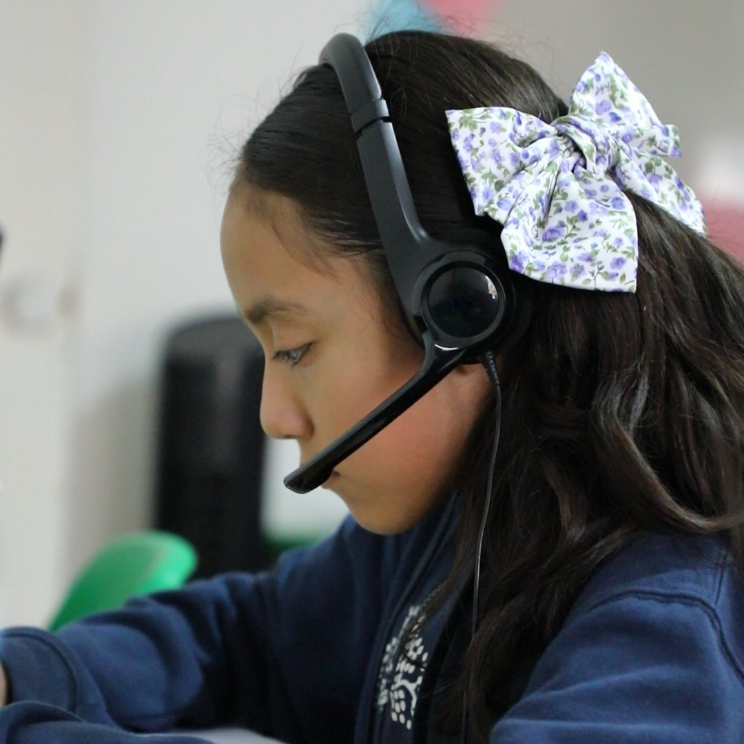 Una alumna de primaria del Instituto Zoe, con sus audífonos y un moño en el cabello, atenta a su clase