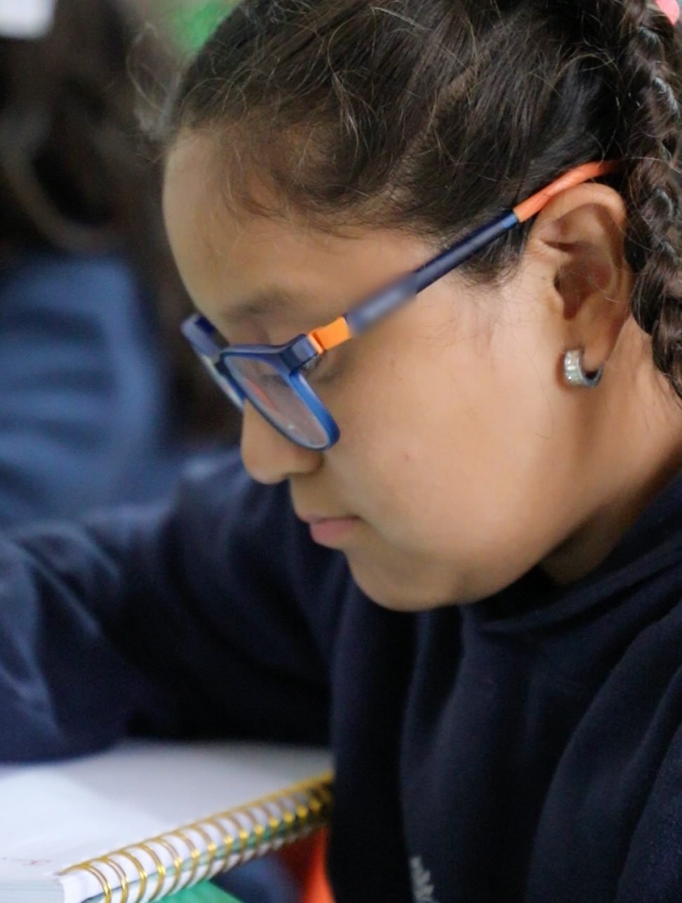 Una alumna de primaria del Instituto Zoe, con lentes, escribe concentrada en su cuaderno